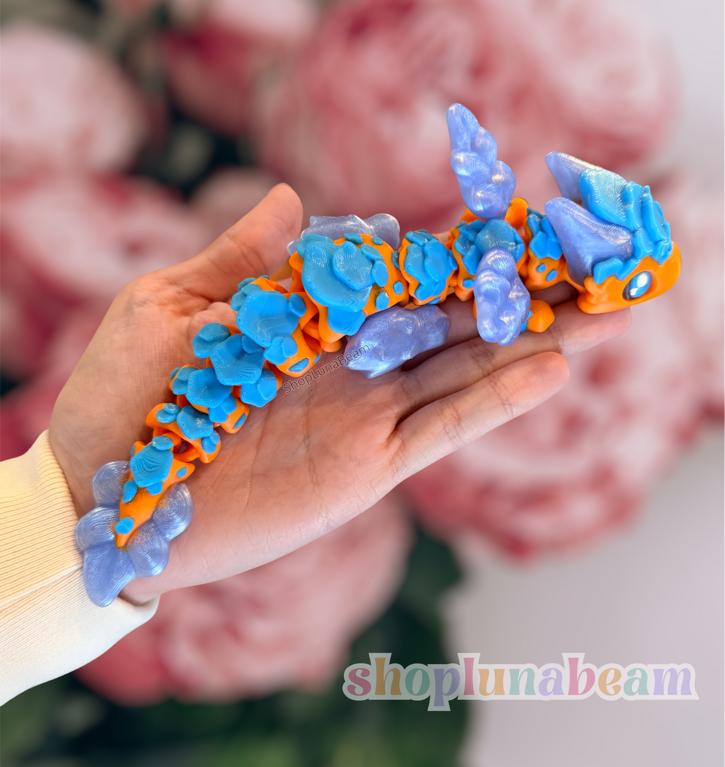 Colorful toy resembling a dragon with blue and orange design held in a hand against a blurred floral background.