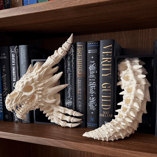 A pair of off-white dragon skull and tail bookends displayed on a wooden bookshelf between books.